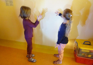 Dwie dziewczynki tworzą cienie ze swoich dłoni na ścianie.